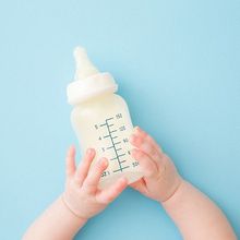 Infant hands holding bottle of milk on light blue floor background.