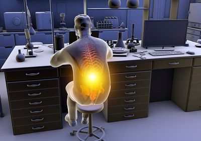 A person slouches while sitting at their laboratory bench, causing musculoskeletal strain, indicated by a yellow highlight on their spine.