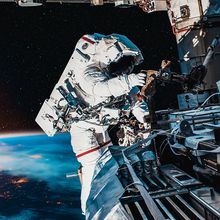 Astronaut working on the space station in outer space, with the Earth and sun in the background.