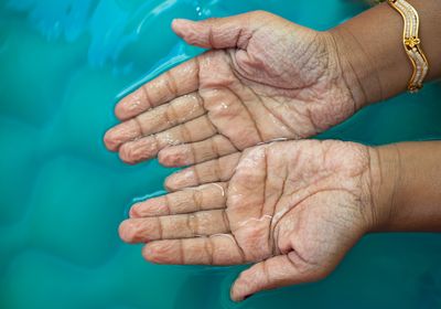 wrinkled hands held over blue water