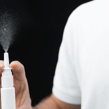 A person in a white shirt activates a nasal spray