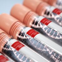 clear blood draw tubes with peach-colored caps and white labels with a red banner that has a DNA double helix icon and the word text. inside the tubes is a conceptual drawing of a DNA double helix in white