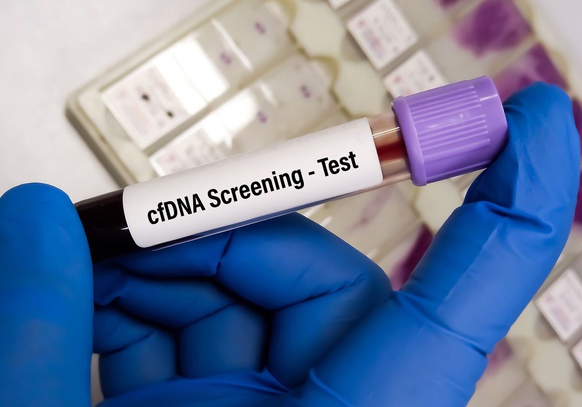 A blood test tube with the label ‘cfDNA Screening–Test’, held in a hand wearing blue gloves.