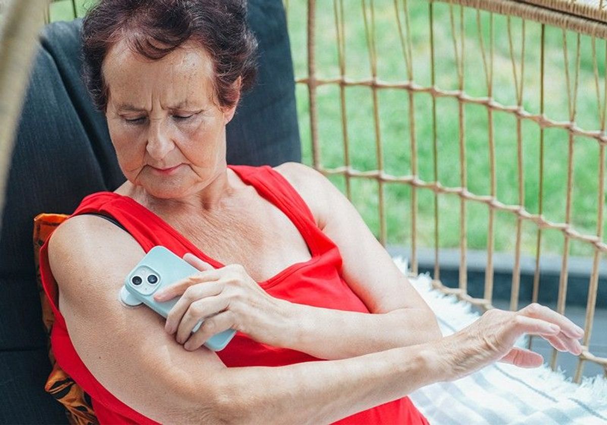 A woman with diabetes checks her blood glucose levels using a wearable biosensor patch on her upper arm, transmitting the results to a smartphone.