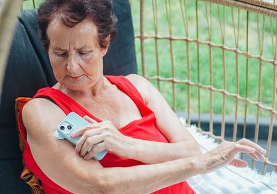 A woman with diabetes checks her blood glucose levels using a wearable biosensor patch on her upper arm, transmitting the results to a smartphone.