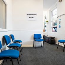 several blue office chairs sit empty in a carpeted room, with a paper sign saying &quot;Vaccination centre welcome&quot; pasted on the white wall&nbsp;above.&nbsp;