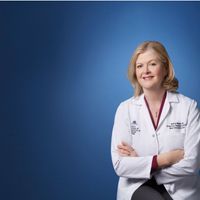 Barbara Murphy wearing a white lab coat, facing the camera with a blue background