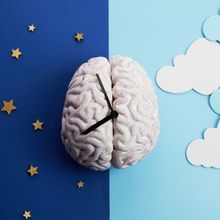 Artistic representation of a brain depicted as a clock on a background with one half in dark blue with yellow stars and one half in light blue with clouds.