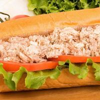 a tuna salad sub with lettuce and tomato on a wooden board with fresh veggies in the background