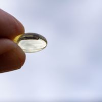 Two fingers grasp a vitamin D capsule